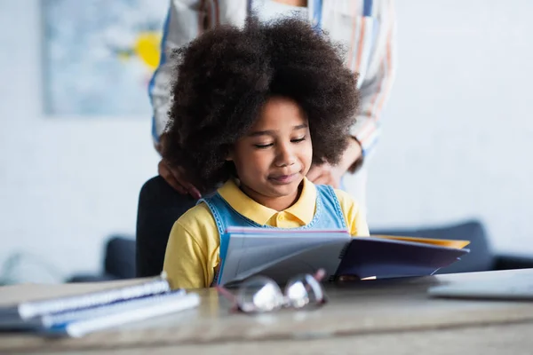 Criança afro-americana olhando para notebook perto mãe turva em casa — Fotografia de Stock