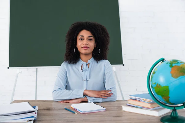 Profesora afroamericana sentada en mesa de trabajo en clase - foto de stock
