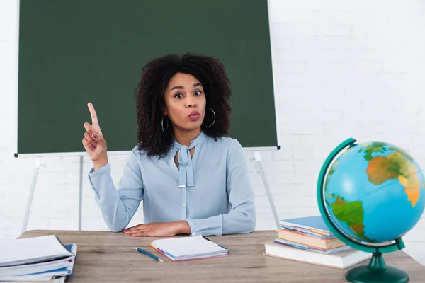 Amazed african american teacher having idea at working table in classroom — Stock Photo