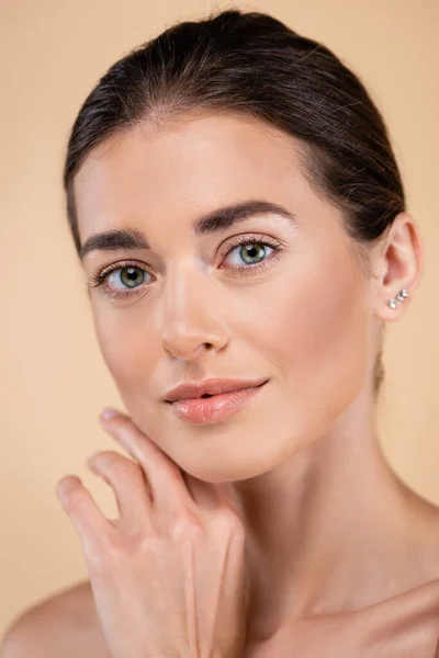 Close up portrait of woman touching face while looking at camera isolated on beige, beauty concept — Fotografia de Stock