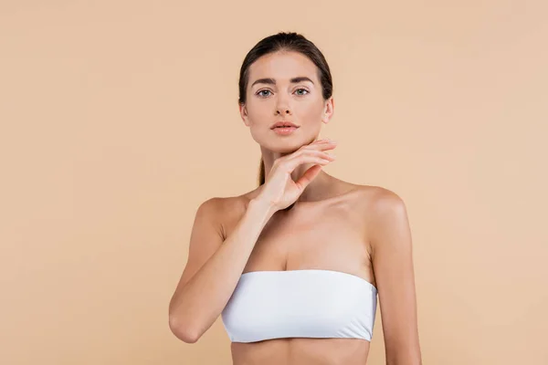 Young woman in white strapless top holding hand near chin isolated on beige, beauty concept — Stock Photo