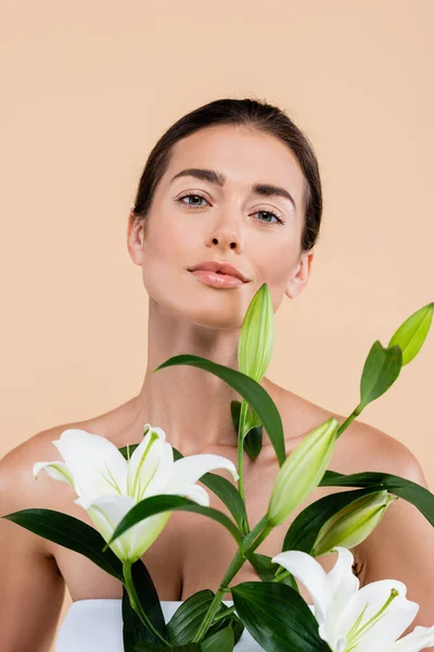 Sensual woman with fresh lily flowers looking at camera isolated on beige, beauty concept — Fotografia de Stock