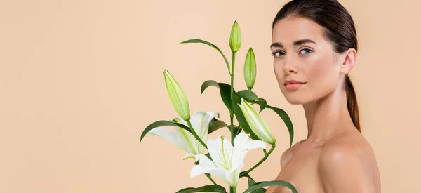 Mujer sensual con hombros desnudos posando con flores de lirio aisladas en beige, concepto de belleza, bandera - foto de stock