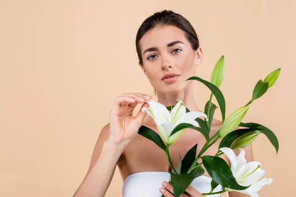 Femme brune avec des fleurs de lys blanc regardant la caméra isolée sur beige, concept de beauté — Photo de stock