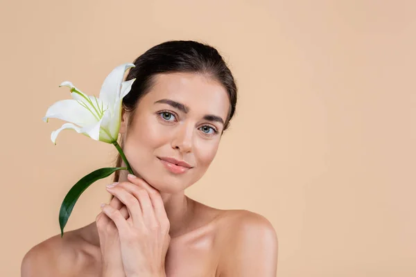 Young woman with naked shoulders holding lily flower near face isolated on beige, beauty concept — Fotografia de Stock