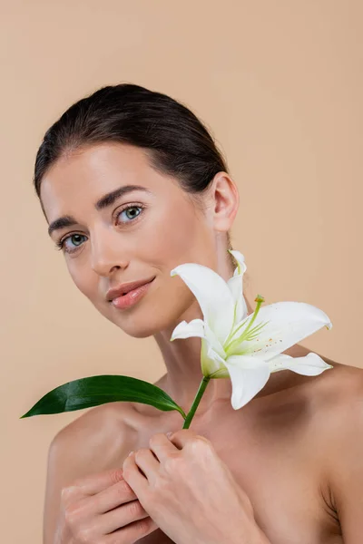 Brünette Frau mit nackten Schultern und weißer Lilie posiert isoliert auf beige, Schönheitskonzept — Stockfoto