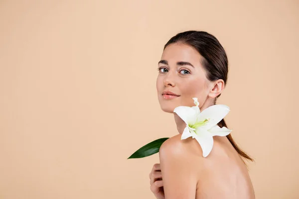 Donna sensuale con giglio bianco fiore sulla spalla nuda guardando la fotocamera isolata sul beige, concetto di bellezza — Foto stock