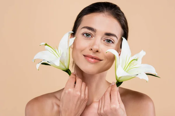 Pleased woman with perfect skin holding lily flowers isolated on beige, beauty concept — Stock Photo