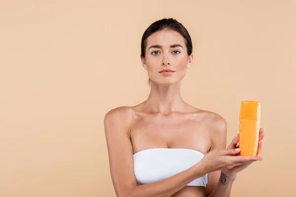 Woman in white strapless top showing bottle of sunblock isolated on beige — Stock Photo