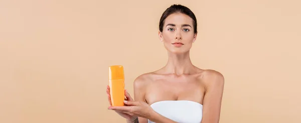 Young woman in strapless top showing bottle of sunblock isolated on beige, banner — Stock Photo