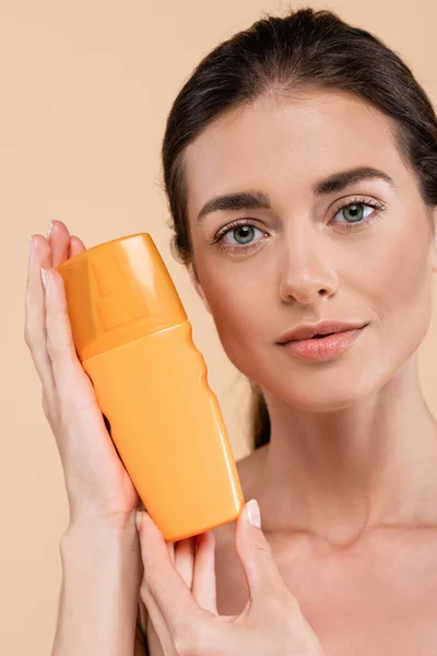 Hübsche Frau zeigt Flasche Sonnencreme, während sie isoliert auf beige in die Kamera schaut — Stockfoto