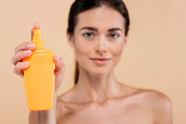 Femme floue tenant vaporisateur bouteille de crème solaire isolé sur beige — Photo de stock
