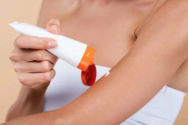 Vista recortada de la mujer que aplica crema protector solar en el brazo aislado en beige - foto de stock