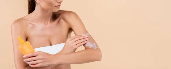 Partial view of woman in strapless top applying sunscreen isolated on beige, banner — Stock Photo