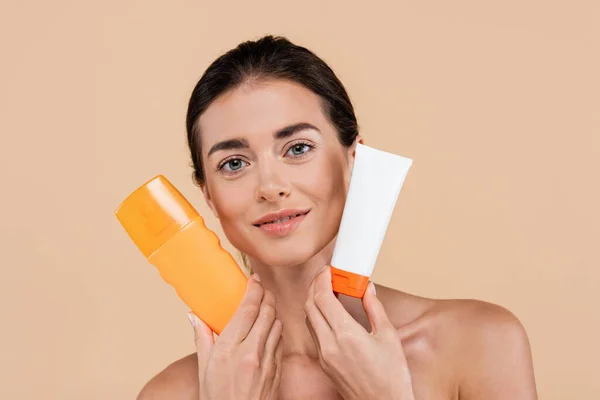 Positive woman showing tube and bottle of sunscreen isolated on beige — Fotografia de Stock