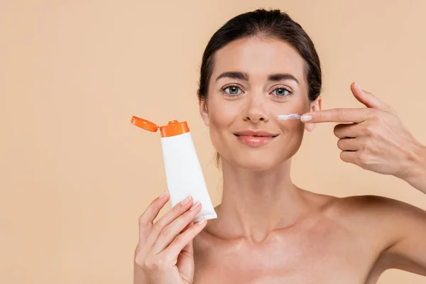 Donna sorridente che applica crema solare sul viso mentre guarda la fotocamera isolata sul beige — Foto stock