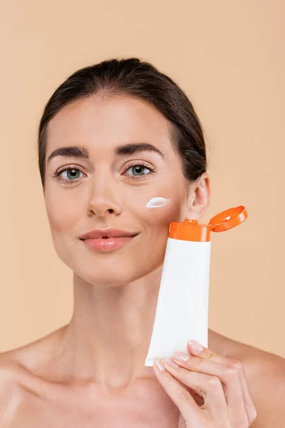 Brunette woman with tube of sunscreen looking at camera isolated on beige — Fotografia de Stock