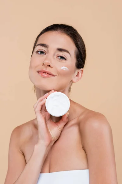 Charmante femme avec trait de crème sur le visage tenant récipient cosmétique isolé sur beige — Photo de stock