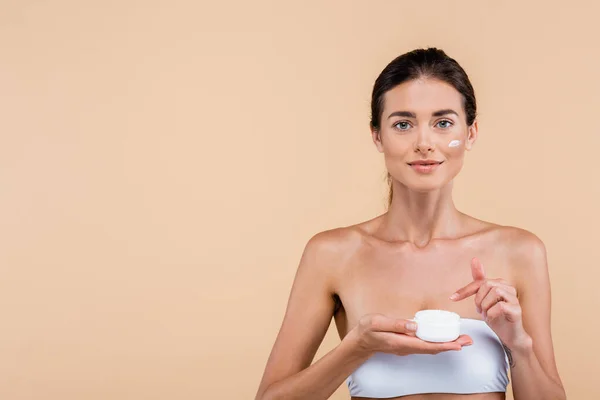 Front view of young woman pointing at cosmetic cream container isolated on beige — Fotografia de Stock