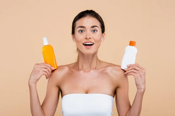 Femme étonnée avec des bouteilles de crème solaire en regardant la caméra isolée sur beige — Photo de stock