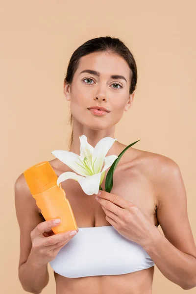 Pretty woman with sunscreen and white lily looking at camera isolated on beige — Fotografia de Stock