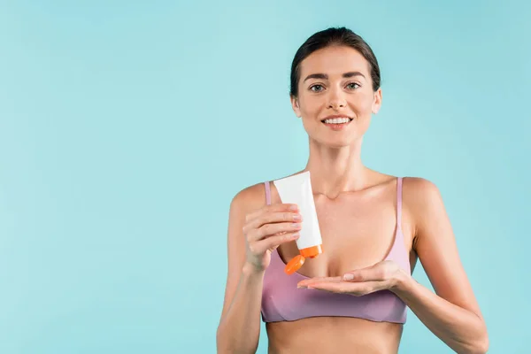 Smiling woman pointing at tube with sunblock while smiling at camera isolated on blue — Fotografia de Stock