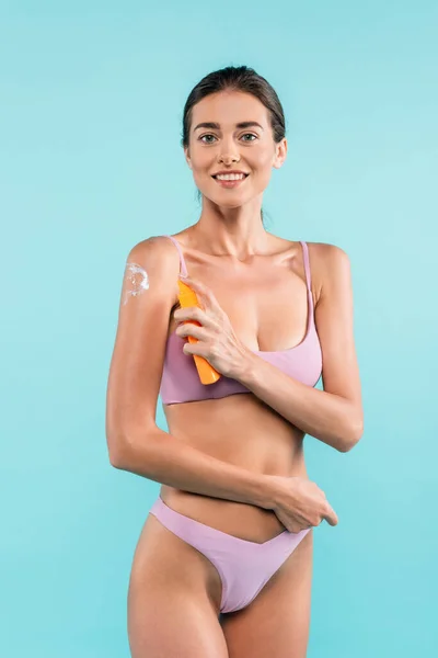 Joyful woman smiling at camera while applying sunscreen isolated on blue — Stock Photo