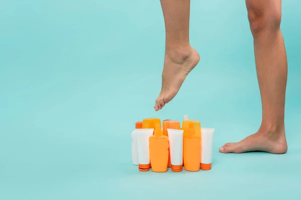 Partial view of female legs near various containers with sunblock on blue — Stock Photo