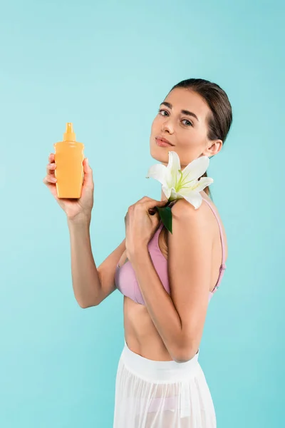 Affascinante donna con crema solare e giglio bianco guardando la fotocamera isolata su blu — Foto stock