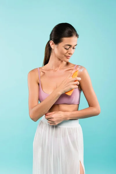 Brunette woman applying sunblock on shoulder isolated on blue — Fotografia de Stock