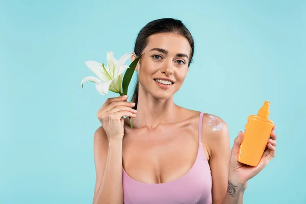 Cheerful woman with sunblock and white lily looking at camera isolated on blue — Stock Photo