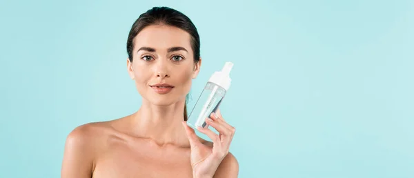 Young woman with naked shoulders holding face tonic isolated on blue, banner — Stock Photo