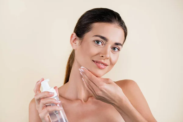 Smiling woman applying face tonic with cotton pad isolated on light beige — Stock Photo