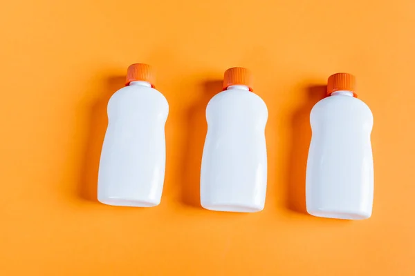 Top view of white bottles with sunscreen on orange background — Fotografia de Stock