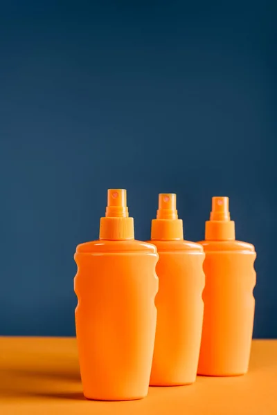 Spray bottles with sunblock on orange surface isolated on blue — Stock Photo