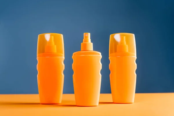 Spray botellas de bloqueador solar en la superficie naranja aislado en azul - foto de stock