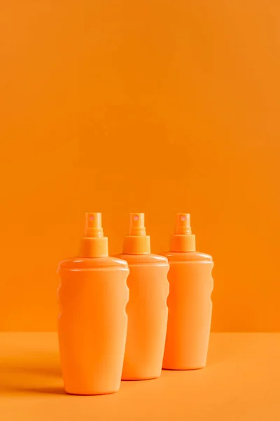 Spray bottles of sunscreen isolated on orange — Stock Photo