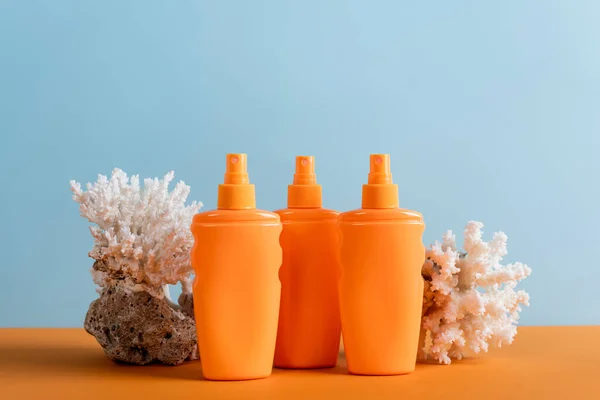 Botellas naranjas de protector solar cerca de corales marinos aislados en azul - foto de stock
