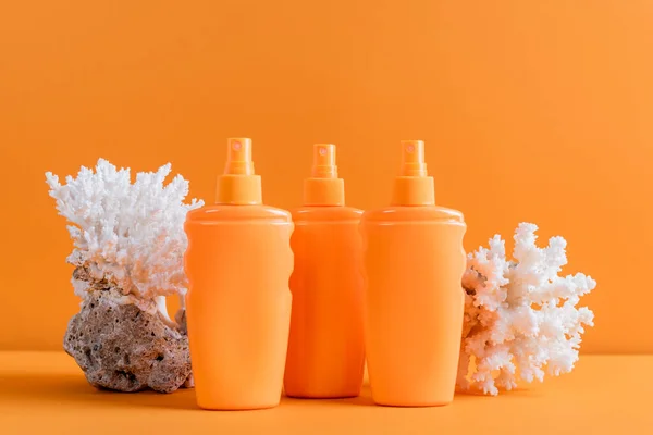 Containers with sunblock near sea corals isolated on orange — Fotografia de Stock