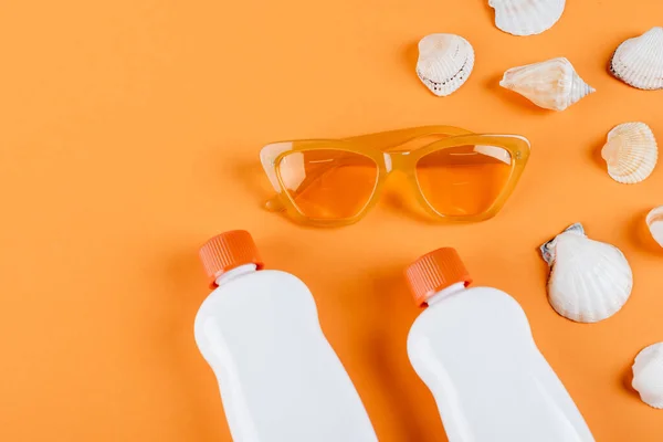 Top view of sunglasses, white sunscreen bottles and seashells on orange surface — Stock Photo