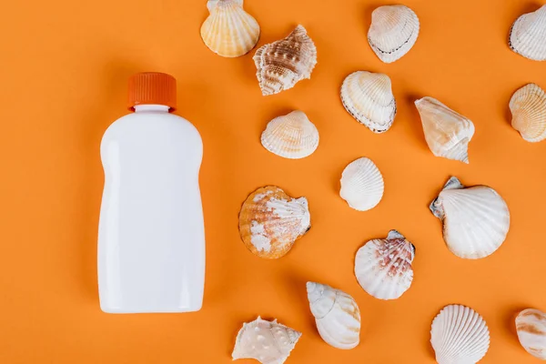 Верхний вид ракушек рядом с белой бутылкой солнцезащитного крема на оранжевой поверхности — стоковое фото