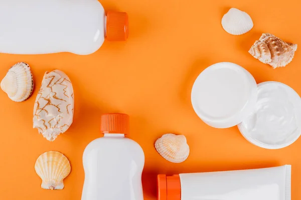 Vue de dessus des coquillages près des conteneurs avec crème solaire et crème cosmétique sur orange — Photo de stock