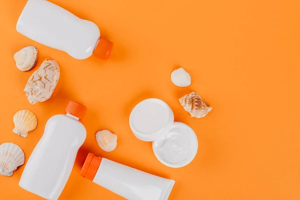 Top view of containers with sunblock near cosmetic cream and seashells on orange — Stock Photo