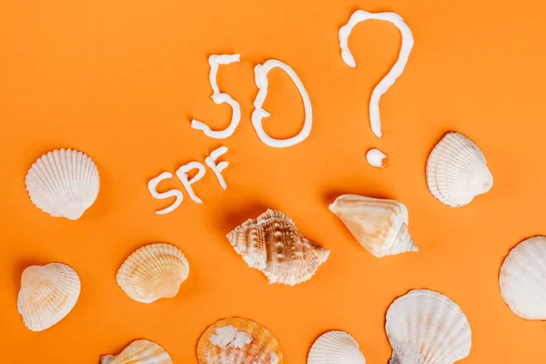 Top view of seashells and number fifty near question mark and spf lettering on orange surface — Stock Photo