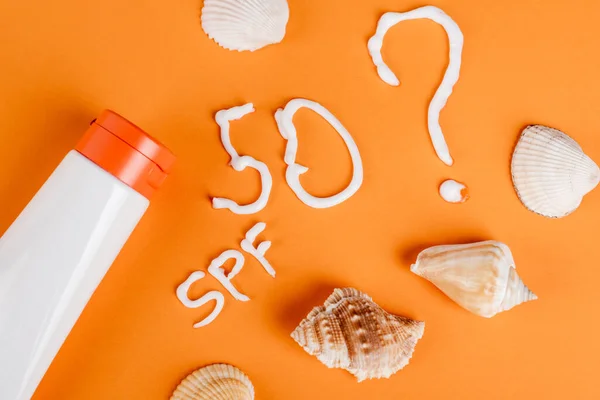 Sonnenschutzmittel in der Nähe von Muscheln, Spf-Schriftzug und Zahl 50 mit Fragezeichen auf orangefarbener Oberfläche — Stockfoto
