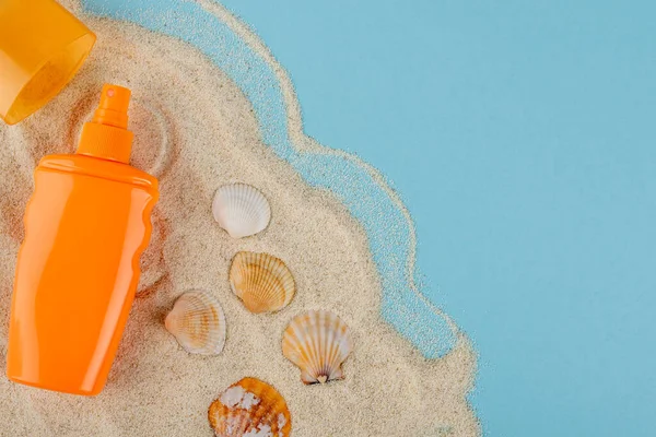 Draufsicht auf orangefarbene Sonnenschutzflasche in der Nähe von Muscheln und Sand auf blauer Oberfläche — Stockfoto