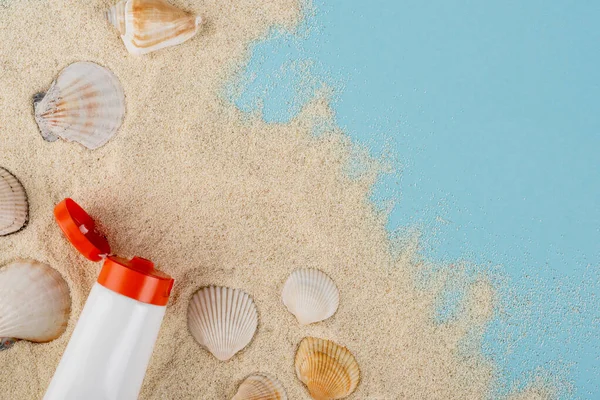 Top view of tube of sunblock and seashells on sand and blue surface — Fotografia de Stock