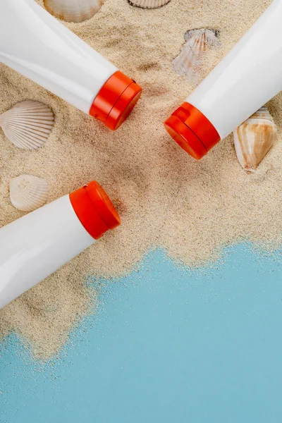 Draufsicht auf Muscheln und Schläuche mit Sonnencreme auf Sand und blauer Oberfläche — Stockfoto