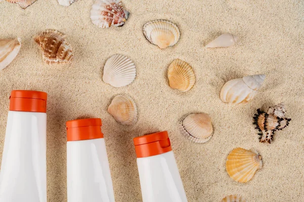 Top view of white tubes with sunblock near seashells on sand — Stock Photo