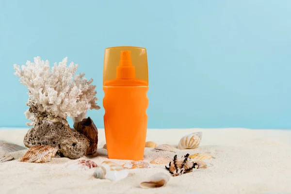 Orangefarbene Flasche Sonnencreme in der Nähe von Muscheln und Korallen auf Sand isoliert auf blau — Stockfoto